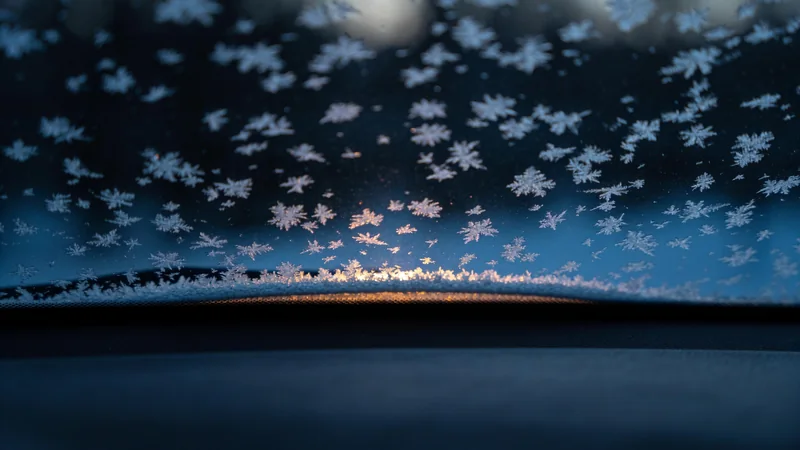 Frost crystals on a car windshield at dawn, seen from inside the car