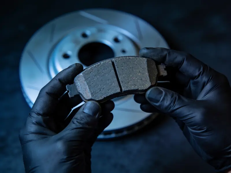 Gloved hands holding up a brake pad for a closer look