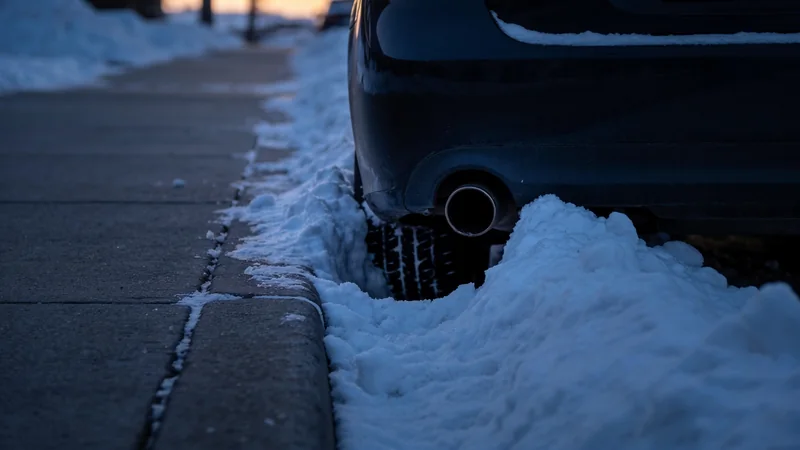 A car's tailpipe just above a snowbank at the curb